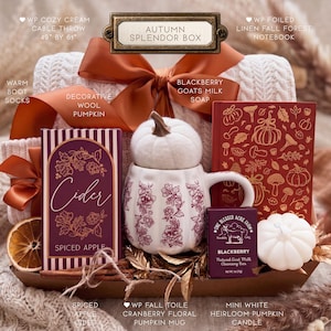 Puede incluir: Una caja de regalo Autumn Splendor que contiene una manta de punto trenzado color crema, una caja de sidra Spiced Apple, una taza blanca con forma de calabaza y motivos florales color ar&aacute;ndano, un cuaderno rojo con motivos forestales dorados, jab&oacute;n de leche de cabra y una vela de calabaza.