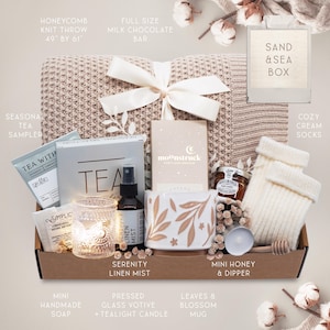 K&ouml;nnte beinhalten: Eine Geschenkbox mit einem Strick-Wurf mit Wabenmuster, einem Tee-Sampler, einer Tasse mit Bl&auml;ttermuster, Mini-Honig, cremefarbenen Socken und anderen Artikeln. Die Box enth&auml;lt eine Tafel Milchschokolade und einen Serenity Linen Mist.