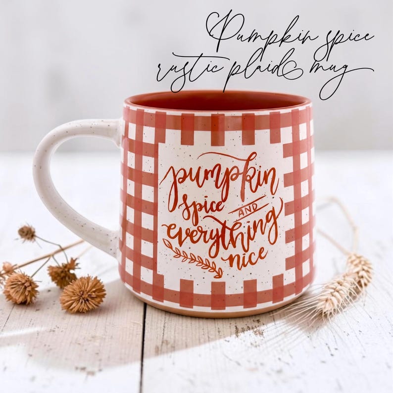 May include: A ceramic mug with a white and orange plaid pattern and a speckled finish. The front features the text "pumpkin spice AND everything nice" in orange cursive script. The interior of the mug is a solid orange color.