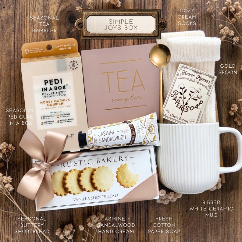 Op de afbeelding: Een geschenkset met een Pedi in a Box honing-havermelkset, een theeproeverijdoos, cr&egrave;mekleurige sokken, een gouden lepel, Flower Market papierzeep, een tube jasmijn- en sandelhout handcr&egrave;me en een doos Rustic Bakery vanille-shortbread koekjes.