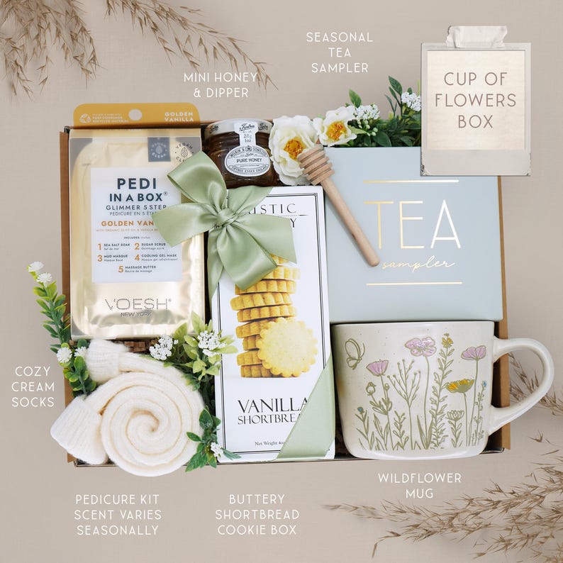 May include: A gift box containing a Pedi in a Box golden vanilla kit, a jar of honey with a wooden dipper, a box of vanilla shortbread cookies tied with a green ribbon, a tea sampler box, a pair of cream socks, and a wildflower patterned mug.