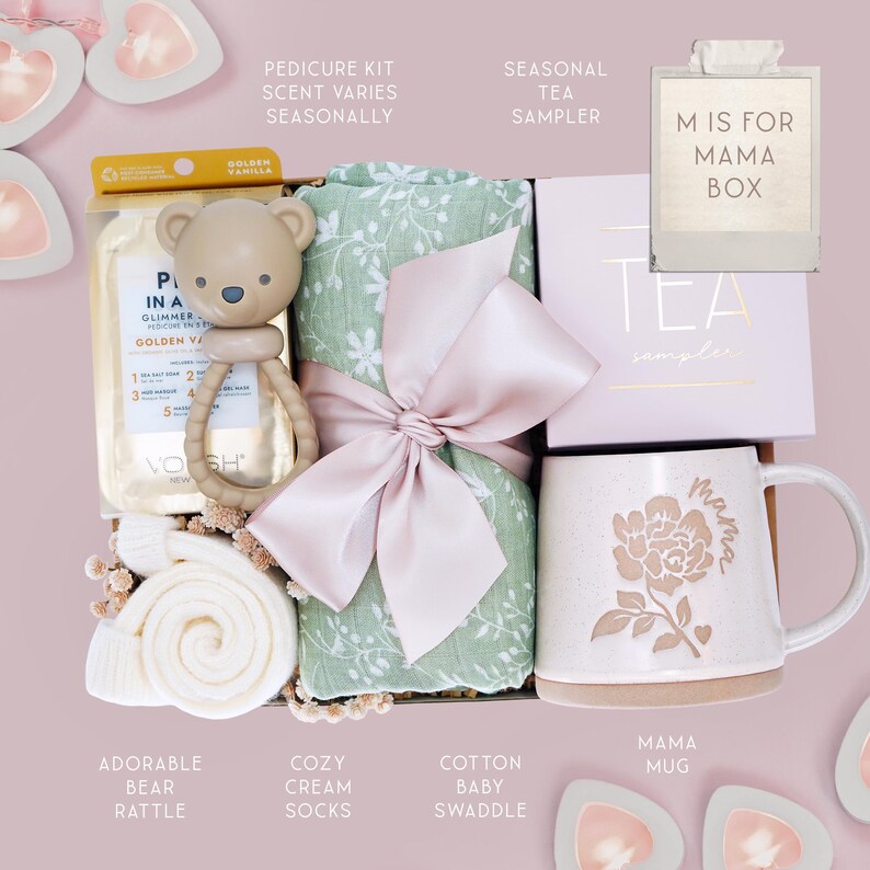 May include: A gift box containing a golden vanilla pedicure kit, a beige bear-shaped rattle, a sage green floral cotton baby swaddle tied with a pink ribbon, a seasonal tea sampler box, and a speckled ceramic mug with a floral mama design.