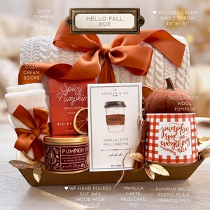 May include: A Hello Fall gift box containing a white cable knit throw measuring 49 inches by 61 inches, cream socks, Spicy Pumpkin tea, a Pumpkin Spice soy wax candle, a Vanilla Latte mug cake mix, a felt pumpkin, and a plaid ceramic mug.