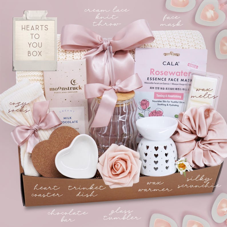 May include: A gift box filled with self-care items. Includes a cream lace knit throw, a face mask, wax melts, a heart-shaped coaster, a trinket dish, a chocolate bar, a glass tumbler, and a wax warmer.
