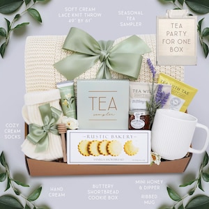 K&ouml;nnte beinhalten: Ein Geschenk-Korb mit einer weichen cremefarbenen Strickdecke (124 cm x 155 cm), Tee-Sampler, Vanille-Shortbread-Keksen, einer gerippten Tasse und anderen Tee-Party-Essentials. Der Korb ist mit einer salbeigr&uuml;nen Schleife gebunden.
