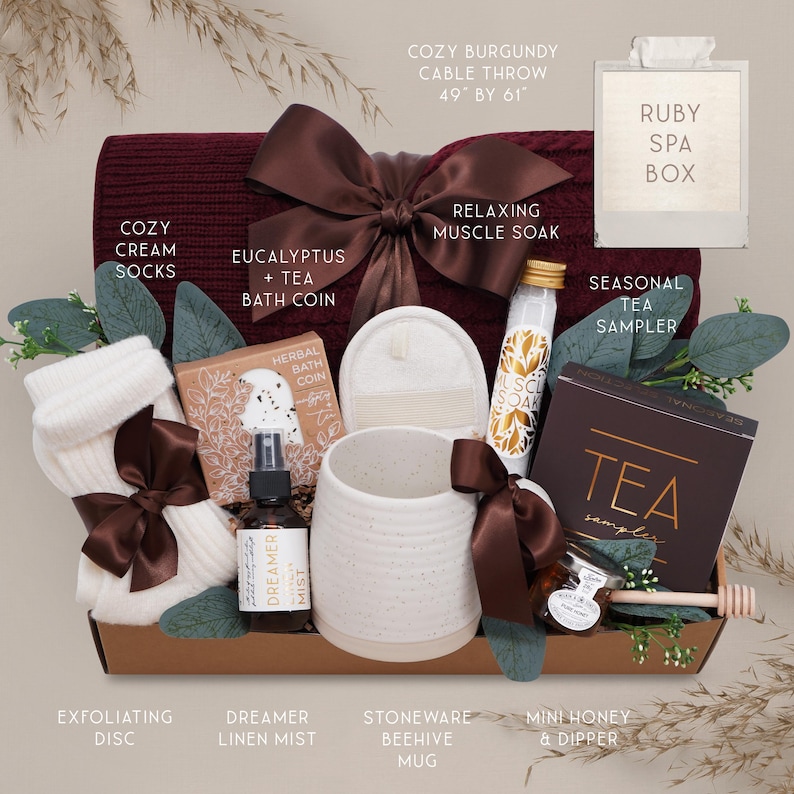 K&ouml;nnte beinhalten: Geschenkbox mit bordeauxfarbenem Strick-Wurftuch (124cm x 155cm), cremefarbenen Socken, einem Steinzeugbecher und anderen Spa- und Tee-Artikeln. Enth&auml;lt Dreamer-Leinen-Nebel, ein Tee-Sampler und einen Mini-Honig-Dipper.