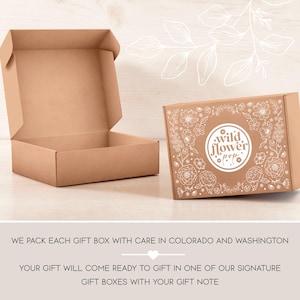 May include: Two light brown cardboard gift boxes. One box is open with an empty interior. The other box is closed and features a white circular logo with the text "wild flower pop" surrounded by intricate white line drawings of various flowers.