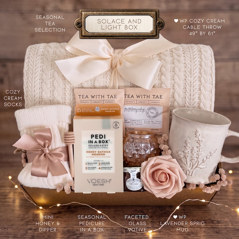Op de afbeelding: Een cadeaupakket met een cr&egrave;mekleurige kabelgebreide deken van 124 bij 155 cm, cr&egrave;mekleurige sokken met een roze lint, een Pedi in a Box set, twee Tea with Tae zakjes, een gefacetteerd glazen votief, honing met een dipper en een lavendel mok.