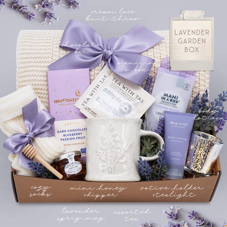 May include: A gift basket with a cream-colored knit throw, lavender-themed items, and a light purple bow. Includes a mug, body lotion, tea, chocolate, cozy socks, honey, and a votive holder. The box is labeled "Lavender Garden Box."