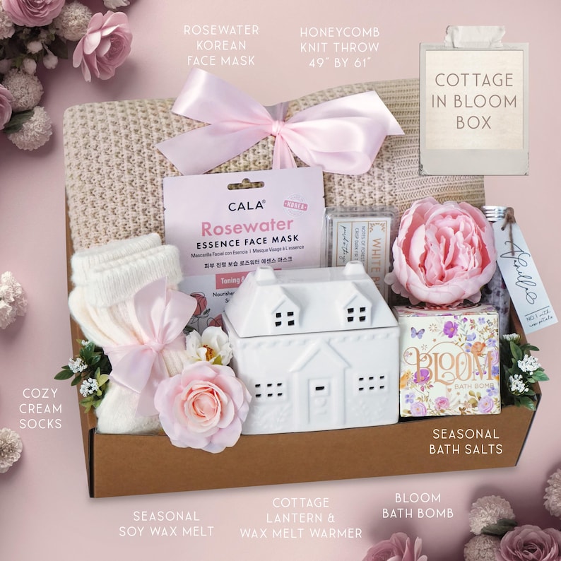 May include: A gift box filled with self-care items. Includes a honeycomb knit throw (49" x 61"), face mask, cozy cream socks, a cottage lantern, seasonal soy wax melt, bath salts, and a bloom bath bomb. Decorated with pink flowers and ribbons.