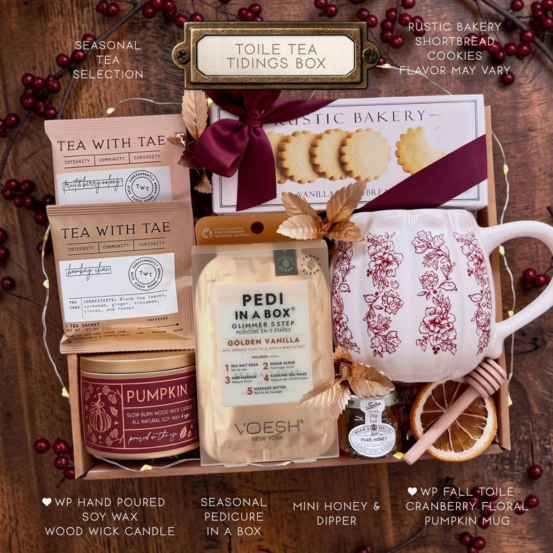 Puede incluir: Una caja de regalo que contiene dos paquetes de t&eacute; Tea With Tae, una caja de galletas de mantequilla Rustic Bakery con cinta granate, un kit de pedicura Voesh, una taza blanca con forma de calabaza y motivos florales rojos, miel, un cuchar&oacute;n y una rodaja de naranja seca.