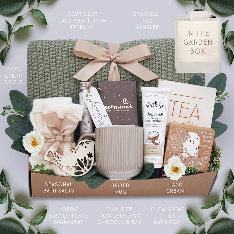 K&ouml;nnte beinhalten: Geschenkbox mit einem salbeigr&uuml;nen Spitzentrickwurf (124cm x 155cm), cremefarbenen Socken, einer gerippten Tasse, einer dunklen Espresso-Schokoladenstange und einem saisonalen Tee-Sampler. Enth&auml;lt einen nordischen Vogelornament, Handcreme und Badesalze.