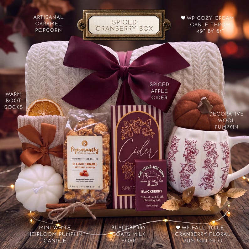 May include: A gift box set containing a cream cable knit throw measuring 49 inches by 61 inches, a white pumpkin-shaped candle, a bag of caramel popcorn, a blackberry goat milk soap bar, a spiced apple cider mix, and a floral pumpkin mug.