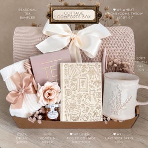 May include: A Cottage Comforts Box gift set containing a 49" by 61" wheat honeycomb throw, a tea sampler, a soft touch gel pen, cream socks with a ribbon, a mini honey jar with a dipper, a linen foiled cottage notebook, and a lavender sprig mug.