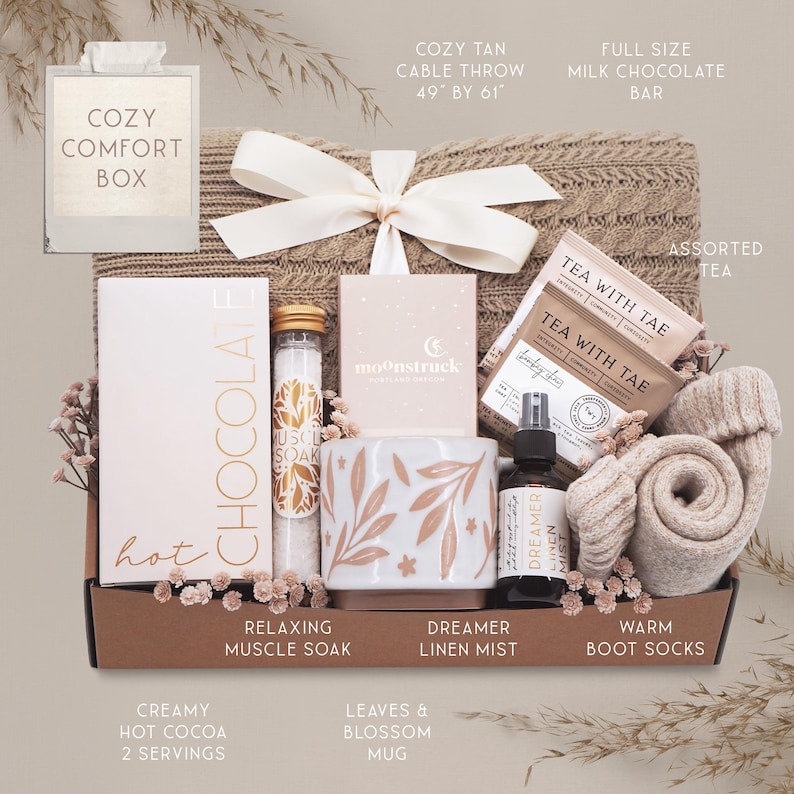 K&ouml;nnte beinhalten: Ein gem&uuml;tlicher Geschenkbox mit Pflegeprodukten. Enth&auml;lt einen beigefarbenen Strickwurf (124cm x 155cm), verschiedene Teesorten, eine Milchschokoladentafel, eine Tasse, Badesalz, Leinen-Mist, warme Stiefelsocken und hei&szlig;e Schokolade.