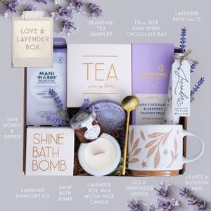 May include: A gift box labeled "Love & Lavender Box" filled with self-care items. Includes a tea sampler, chocolate bar, bath salts, manicure kit, bath bomb, candle, honey, spoon, and a mug with a floral design. The box is decorated with lavender sprigs.