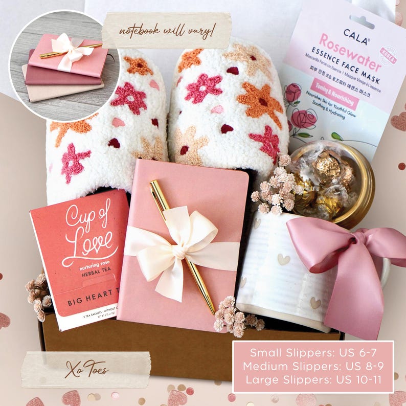 May include: A gift box with a pink theme, containing a notebook, pen, slippers, tea, face mask, mug, and chocolates. The slippers are white with floral embroidery. The notebook has a bow and a gold pen. The tea box reads "Cup of Love".
