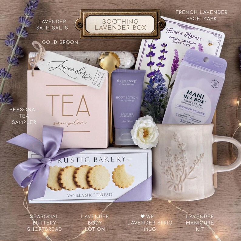 May include: A gift box set labeled Soothing Lavender Box containing a pink tea sampler box, a gold spoon, a tube of lavender body lotion, a French lavender face mask, a lavender manicure kit, and a mug with a lavender sprig design.