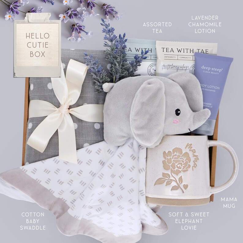 May include: A gift box containing a gray polka dot swaddle with a cream ribbon, a plush gray elephant lovie, a speckled ceramic mug with a floral design and the word Mama, a tube of lavender chamomile lotion, and tea packets.