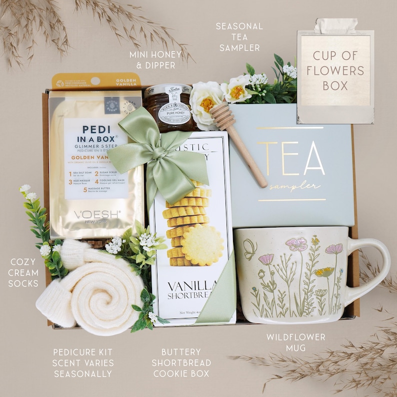 May include: A gift box with a variety of items, including a pedicure kit, honey, shortbread cookies, tea sampler, and a wildflower mug. The box is decorated with a green bow and includes cozy cream socks.