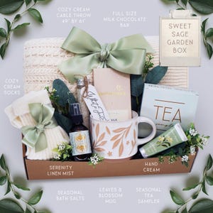 May include: A Sweet Sage Garden Box gift set containing a cream cable throw measuring 49 by 61 inches, a milk chocolate bar, a pair of cream socks, a bottle of serenity linen mist, a mug with leaf patterns, tea samples, hand cream, and bath salts.