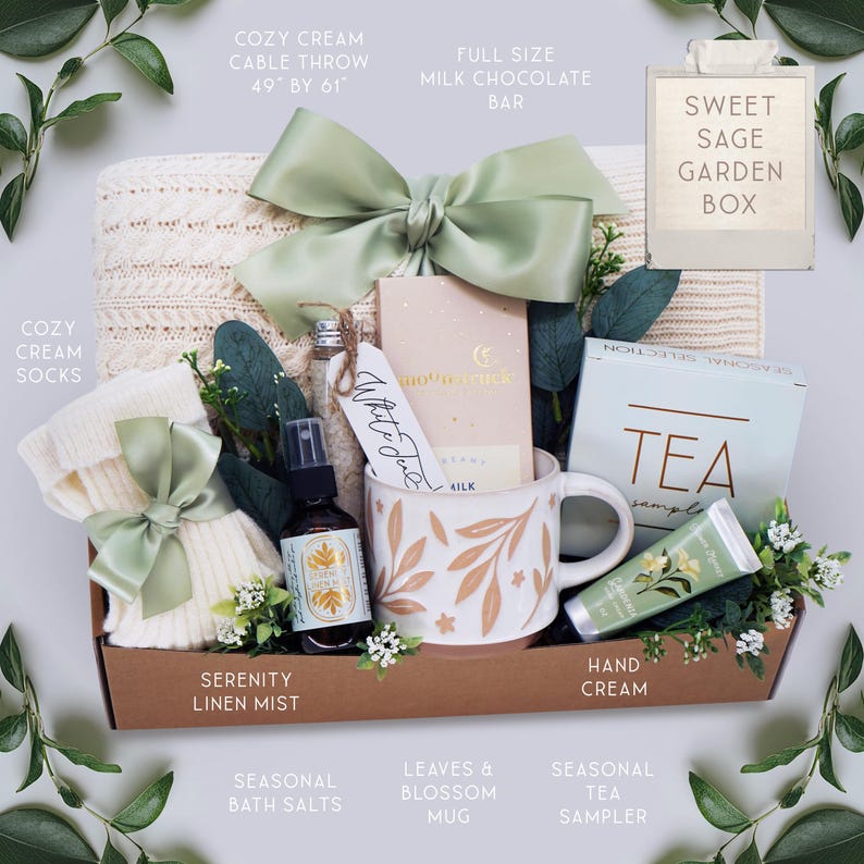 May include: A Sweet Sage Garden Box gift set containing a cream cable throw measuring 49 by 61 inches, a milk chocolate bar, a pair of cream socks, a bottle of serenity linen mist, a mug with leaf patterns, tea samples, hand cream, and bath salts.