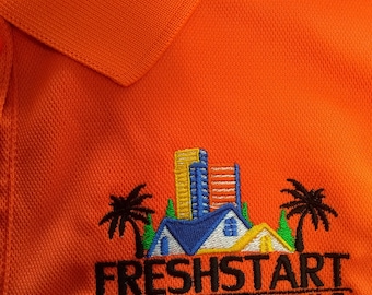 May include: Orange polo shirt with an embroidered logo that says "FRESHSTART DEVELOPMENT CGC 1513935". The logo features a stylized cityscape with palm trees and houses.