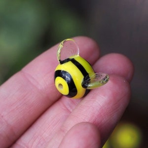 Puede incluir: Una cuenta de vidrio amarilla y negra con forma de abeja con alas de vidrio transparente.