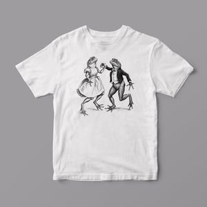 May include: White t-shirt with a black and white illustration of two frogs dancing. The female frog is wearing a dress and the male frog is wearing a tuxedo.