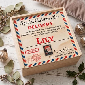 May include: A square wooden box with a sliding lid featuring a printed design of a Christmas Eve delivery parcel. The lid has red and blue diagonal stripes along the border, the text Special Christmas Eve DELIVERY, the name LILY, and a Santa stamp.