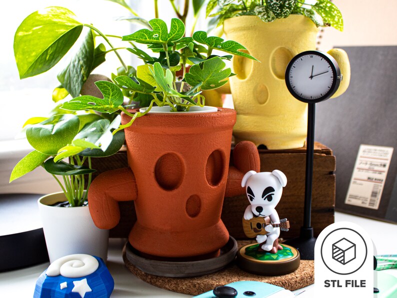 May include: Two terracotta-coloured plant pots with cartoon faces, one with a yellow face and the other with a brown face. A white dog figurine with a guitar is in front of the pots. A black clock with white hands is on a black stand. The text "STL FILE" is on a white background with a grey cube icon.