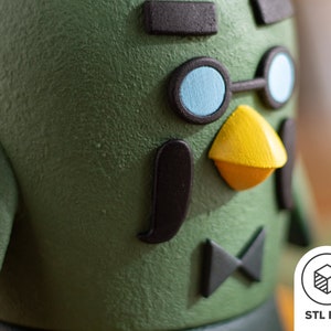 Pu&ograve; includere: Primo piano di una statuetta verde stampata in 3D con occhiali neri, un becco giallo e un papillon nero. La statuetta ha una superficie testurizzata.