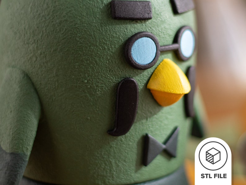 Pu&ograve; includere: Primo piano di una statuetta verde stampata in 3D con occhiali neri, un becco giallo e un papillon nero. La statuetta ha una superficie testurizzata.
