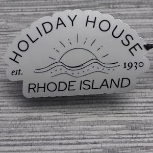 May include: A white sticker with black text and a graphic of a sun setting over a wavy ocean. The text reads "HOLIDAY HOUSE est. 1930 RHODE ISLAND".