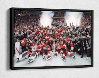 May include: A group of hockey players in red and white uniforms celebrate on the ice after winning the Stanley Cup. The players are holding the trophy and are surrounded by confetti and cheering fans.
