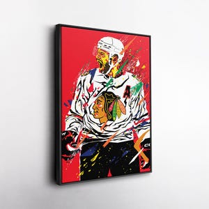 Op de afbeelding: Een ingelijste kunstdruk van een hockeyspeler in een wit en zwart shirt met nummer 4. Het kunstwerk heeft een rode achtergrond met kleurrijke verfspattereffecten. De speler draagt een witte helm en zwarte handschoenen.