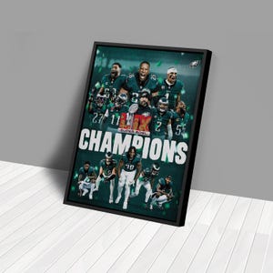 May include: A black framed poster with a green and white design featuring a group of football players celebrating. The players are wearing green and white uniforms and holding a trophy. The text "Champions" is printed in white letters on a green background. The text "Super Bowl" is printed in white letters on a red background.