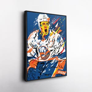 May include: Framed pop art print of a hockey player in a white, blue, and orange uniform. The player is wearing a helmet with the number 13. The background is blue with colourful abstract elements. The print is in a black frame.