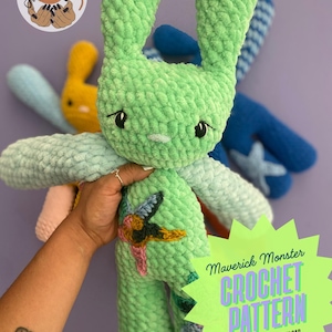 Può includere: Un grande coniglietto all'uncinetto verde chiaro con lunghe orecchie e un viso cucito. Il coniglietto ha accenti azzurri e rosa sulle braccia e un colorato disegno ricamato sul petto. L'immagine include anche una grafica a stella verde con il testo "Maverick Monster CROCHET PATTERN PDF DIGITAL DOWNLOAD."