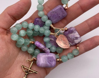 May include: A green and purple beaded rosary with a gold crucifix and a charm featuring the Virgin Mary. The beads are made of agate and amethyst.