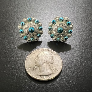 May include: A pair of silver earrings with a circular design featuring blue rhinestones.