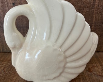 May include: A white ceramic swan figurine with a crackled glaze finish. The swan has a long neck and a wide wingspan. It is a decorative piece for the home.