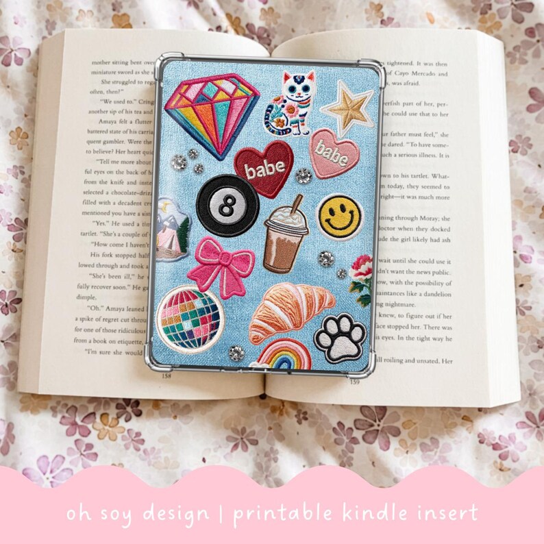 May include: A clear Kindle case insert with a light blue denim-like background, adorned with colorful patches. Patches include a rainbow diamond, a cat, stars, hearts with "babe" text, an 8-ball, a bow, a coffee cup, a smiley face, a globe, a croissant, a rainbow, and a paw print.