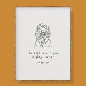 May include: A framed print with a minimalist line drawing of a lion's head. The artwork includes the text "The Lord is with you, mighty warrior" and "Judges 6:12". The frame is a light brown colour, with a white background.