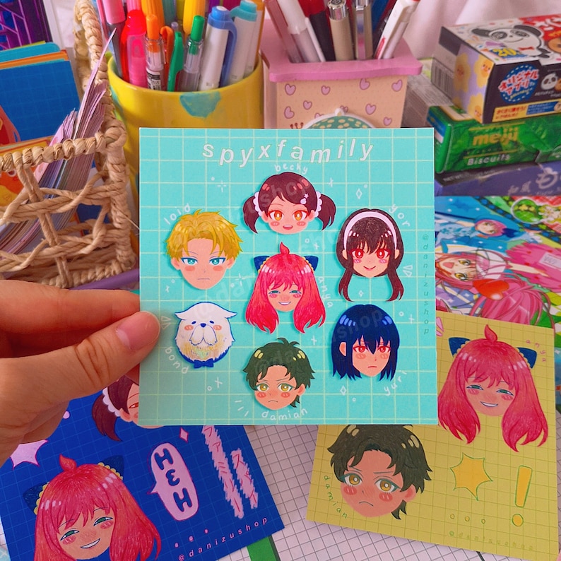 May include: A set of colorful stickers featuring characters from the anime Spy x Family. The stickers are on a light blue background with white grid lines. The characters include Anya, Loid, Yor, Bond, Becky, and Damian.