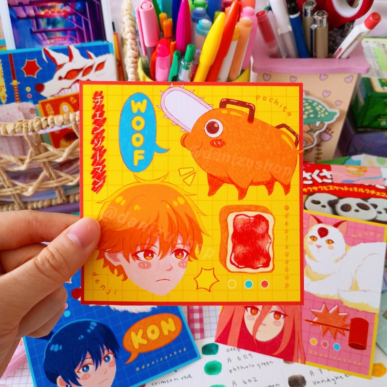May include: A yellow sticker with a cartoon character with orange hair and a red and white shirt. The character is labeled "Denji". The sticker also features a cartoon pig with a chainsaw, labeled "Pochita", and a slice of bread with red jam. The sticker has the text "WOOF" in a speech bubble and the text "Chainsaw Man" in Japanese.