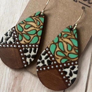 May include: A pair of teardrop-shaped wooden earrings with a geometric pattern. The earrings are made of wood and painted with a variety of colors, including brown, black, white, and teal. The earrings are accented with small white dots.