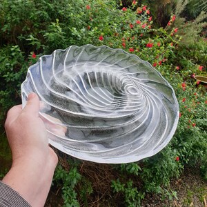 Puede incluir: Un plato de servir de vidrio transparente con un diseño en espiral. El plato está hecho de vidrio grueso y tiene un acabado liso y pulido.