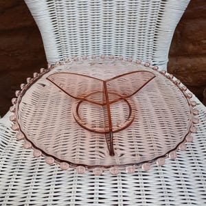Peut inclure: Un plat de service vintage en verre rose à trois compartiments. Le plat a un bord festonné avec de petits détails ronds. Le centre a une conception à trois sections, parfaite pour servir des collations ou des apéritifs.