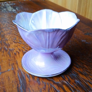 Peut inclure: Un plat à dessert en céramique violet et blanc avec un bord festonné et un piédestal. Le plat a un motif floral et une bordure dorée.